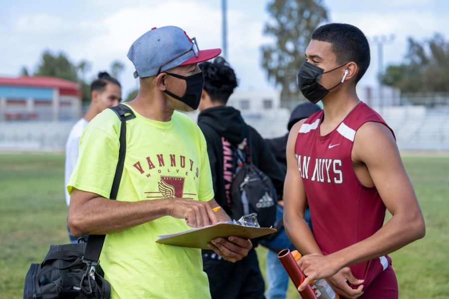 Track and Field Coach Fernando Fernandez speaks to runner Uriel Ruiz after a relay race. Both are wearing masks and following covid-19 guidelines.