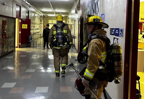 Los Angeles Fire Department firefighters dressed in full turnout gear enter Van Nuys High School as the school’s fire alarms continue to blare on and off. 