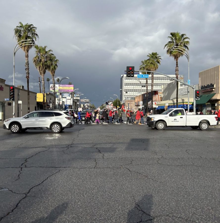 An outsider perspective shows teachers and faculty members walking in a straight line across Van Nuys street.