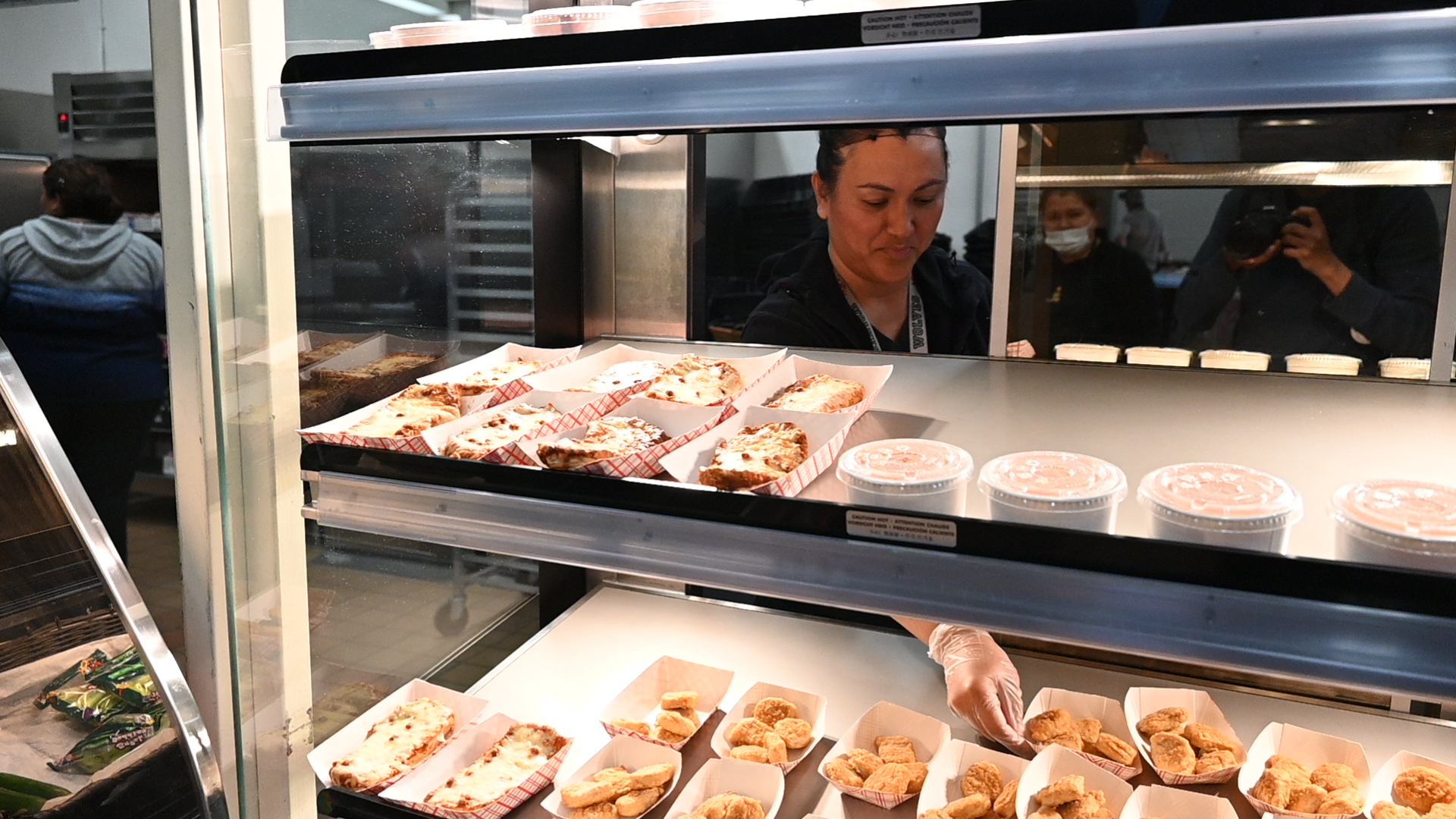 Cafeteria worker Celeste Morales serves up chicken nuggets, cheesy garlic bread with sausage and chicken mashed potato gravy bowls for lunch in the school's cafeteria.