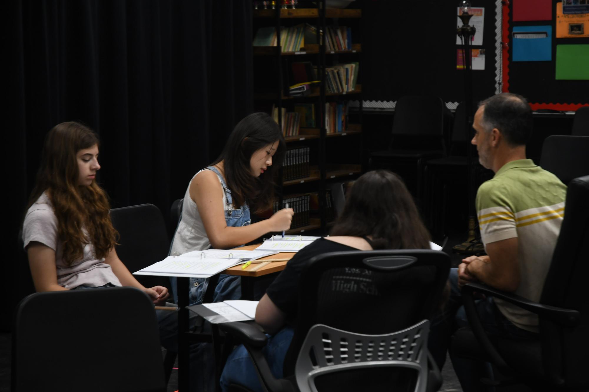 (From L to R) Sophomore Olivia Klipstine, Senior April Cho, Senior Madison Thacker, and Director Mr. Justin Baldridge sit down to work through the meaning of the dialogue in a particular scene.