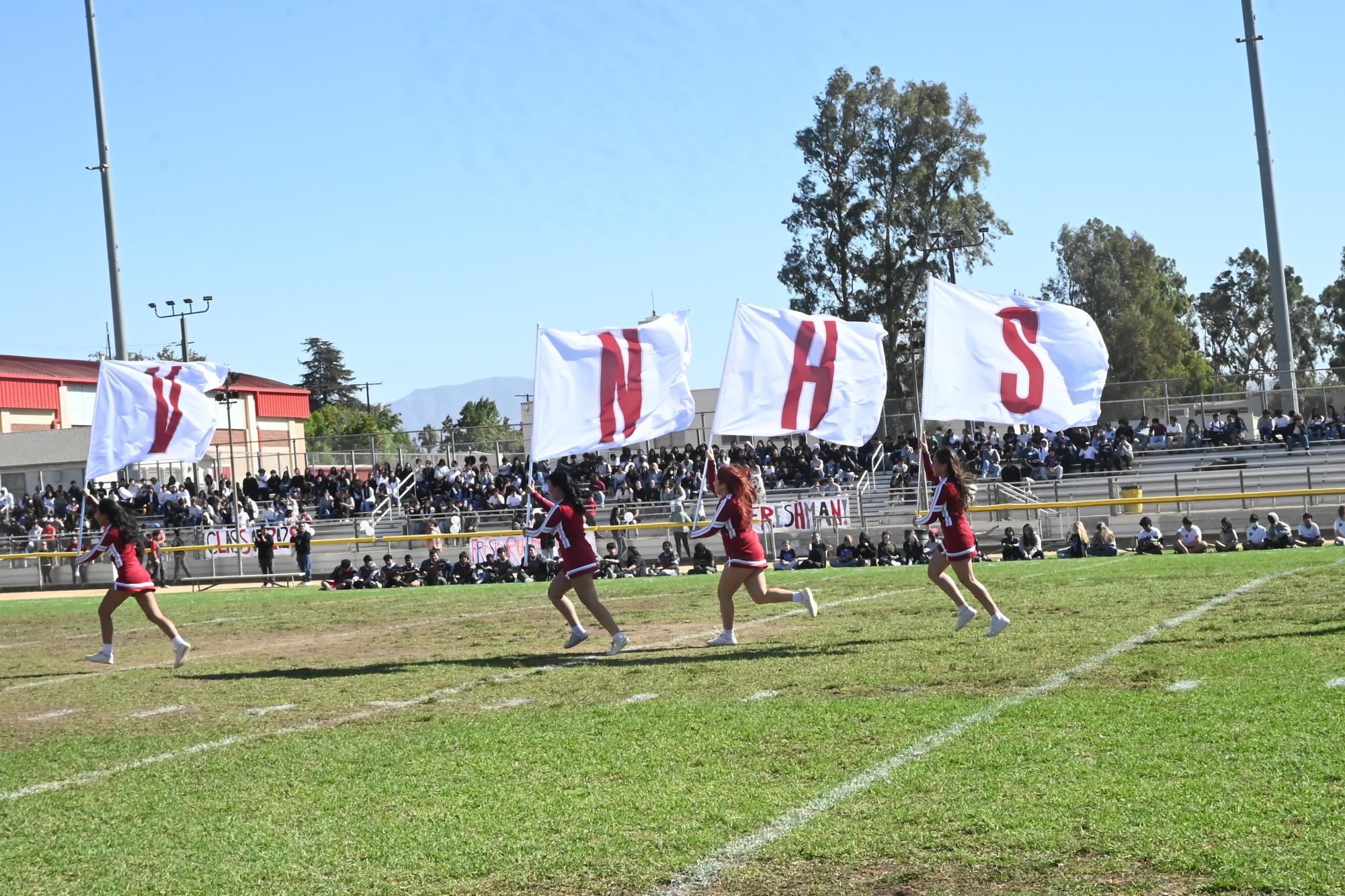 After performing multiple routines, the cheer team sprints across the field, carrying flags that spell out the school's name, "VNHS". 